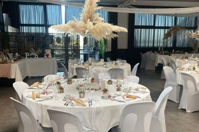Salle de réception décorée avec des tables dressées, nappes blanches, chemins de table en jute et chaises noires.