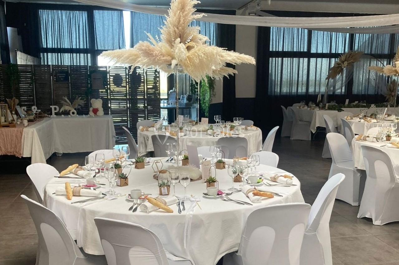 Salle de réception décorée avec des tables rondes dressées, nappes blanches et centre de table en herbes de pampa.