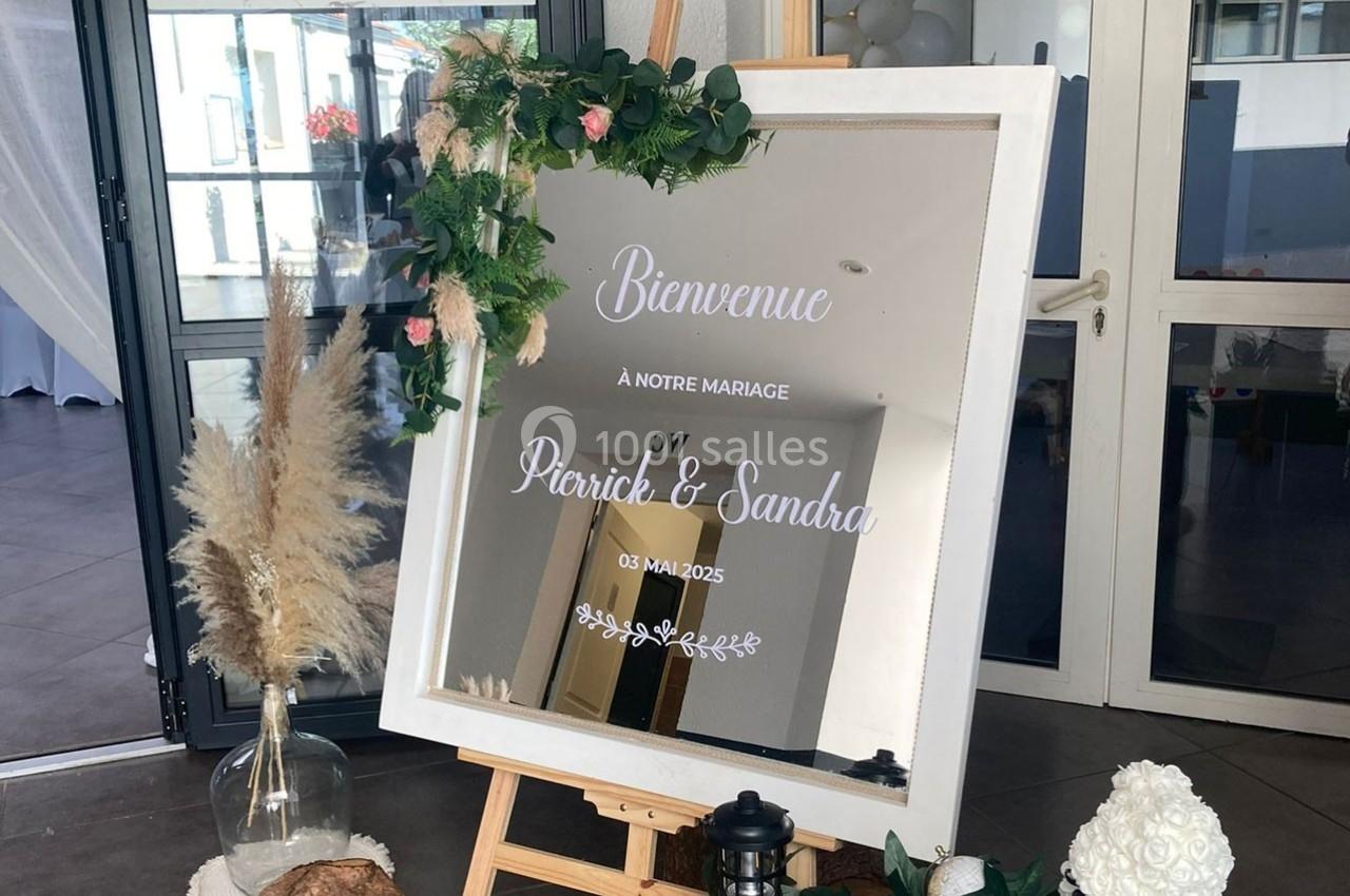 Miroir décoratif sur chevalet avec message de bienvenue pour un mariage, entouré de fleurs et d'éléments naturels.