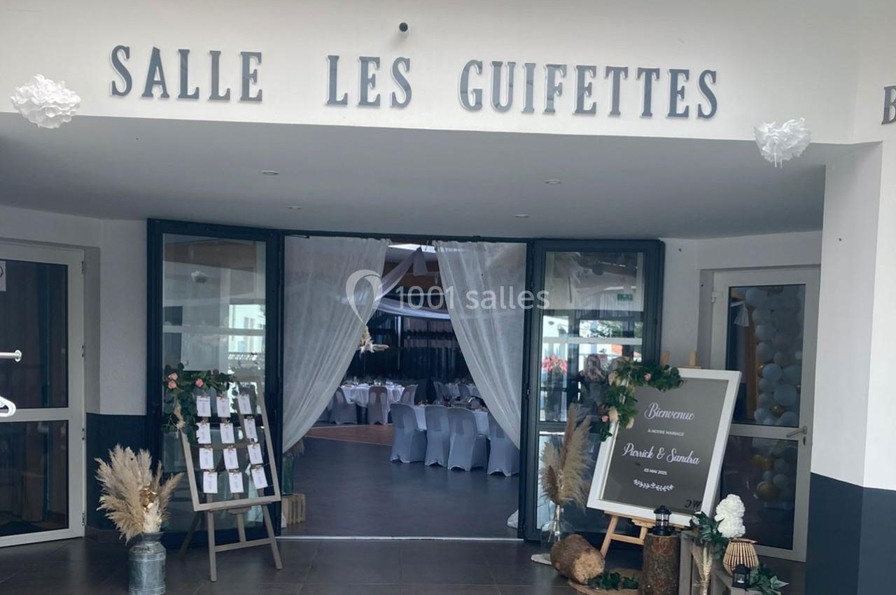 Entrée décorée de la salle ’Les Guifettes’ avec des rideaux blancs, des fleurs et un panneau de bienvenue.