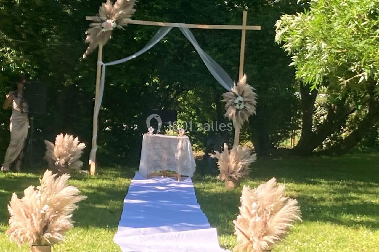 Arche de cérémonie en bois décorée de voilages et de fleurs séchées, installée sur une pelouse en plein air.