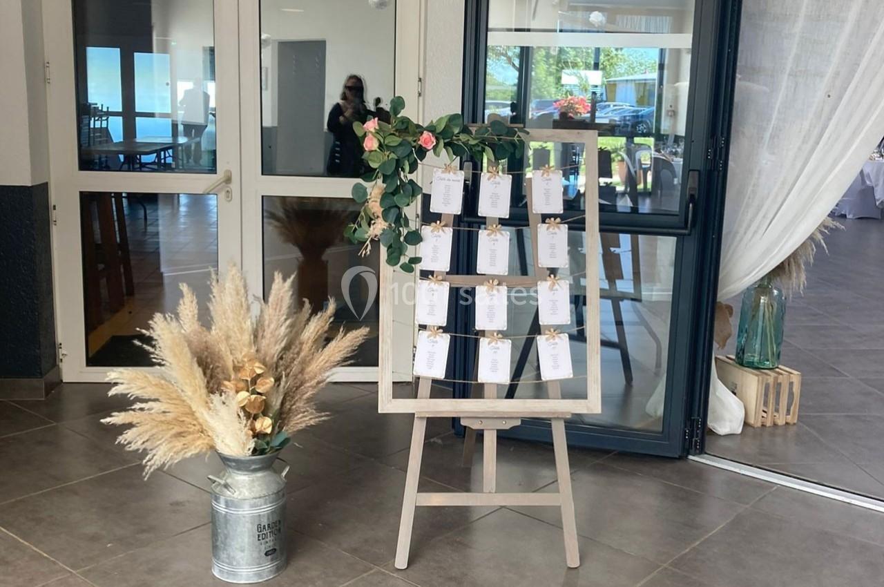 Un plan de table décoratif avec des cartes suspendues, entouré de fleurs et de pampas, dans une salle lumineuse.