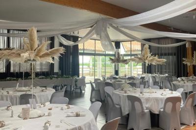 Salle de réception décorée avec des tables dressées, nappes blanches, chemins de table en jute et chaises noires.