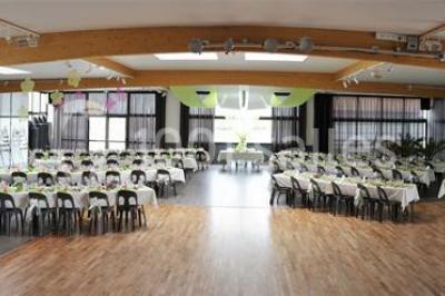 Salle de réception décorée avec des tables dressées, nappes blanches, chemins de table en jute et chaises noires.