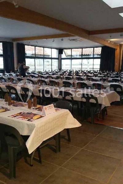 Salle aménagée avec de longues tables dressées pour un repas, disposées en rangées dans un espace lumineux.