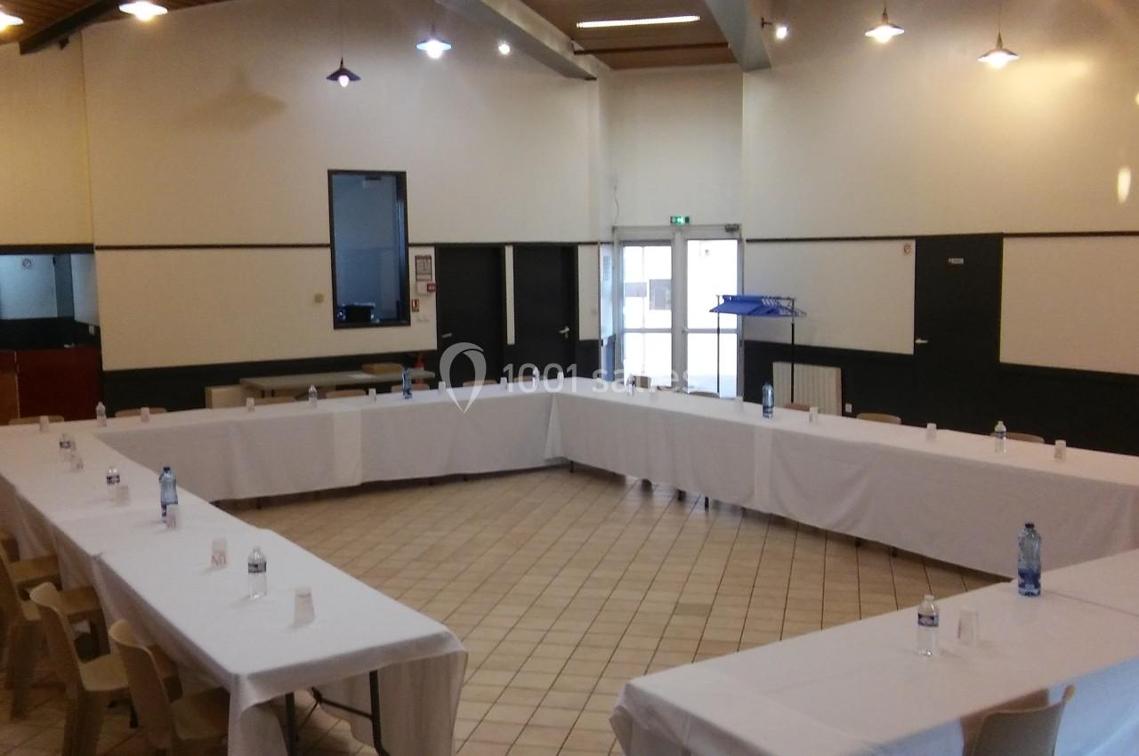 Salle de réunion avec tables disposées en U, nappées de blanc, chaises en bois et éclairage suspendu.