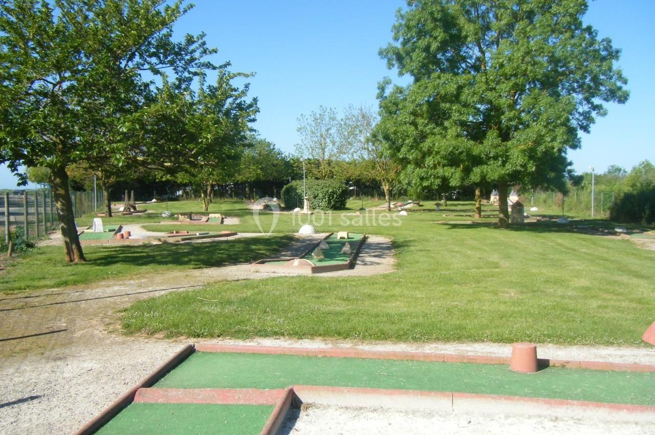 Terrain de mini-golf en plein air avec pelouse, arbres et parcours délimités par des bordures colorées.