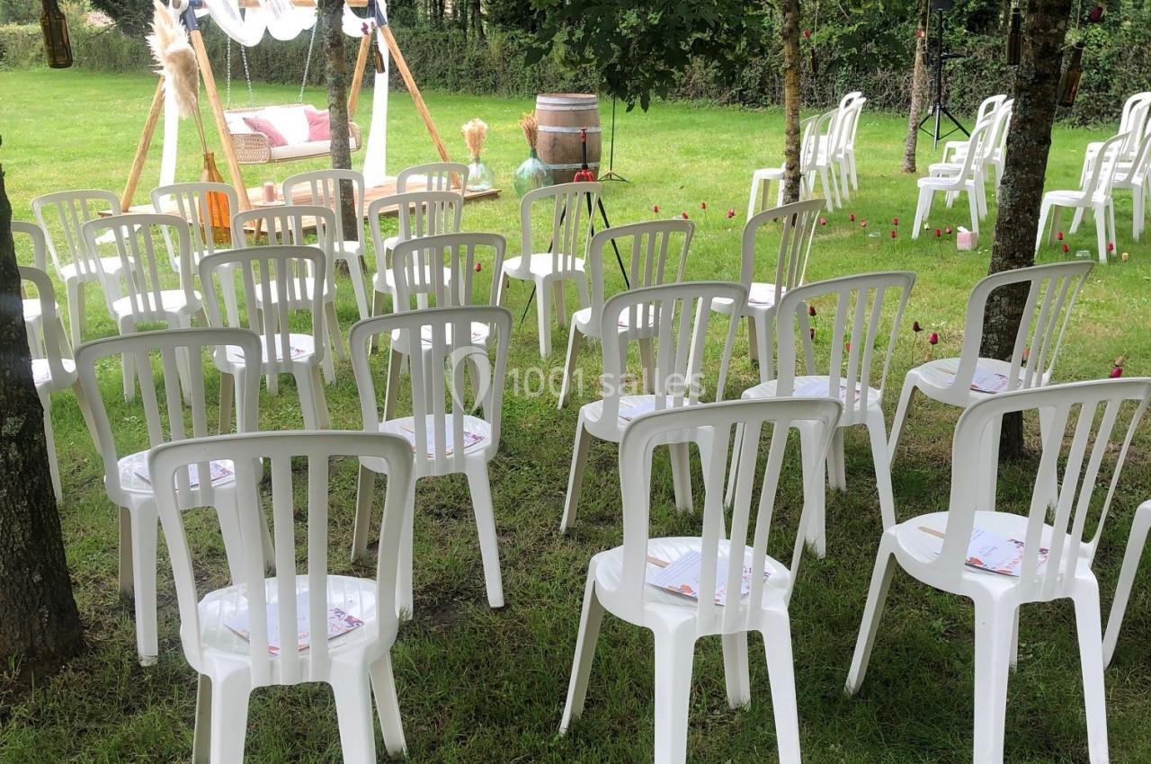 Chaises blanches en plastique disposées en rangées sur une pelouse, face à une arche décorée pour une cérémonie en plein air.
