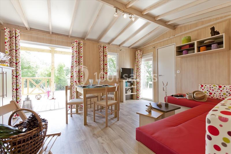 Salon lumineux avec canapé rouge, table à manger en bois, étagères colorées et vue sur une terrasse extérieure verdoyante.