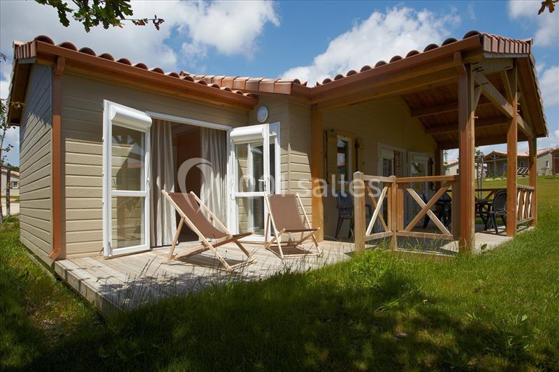 Chalet en bois avec terrasse, deux chaises longues et mobilier de jardin, entouré de pelouse sous un ciel partiellement…