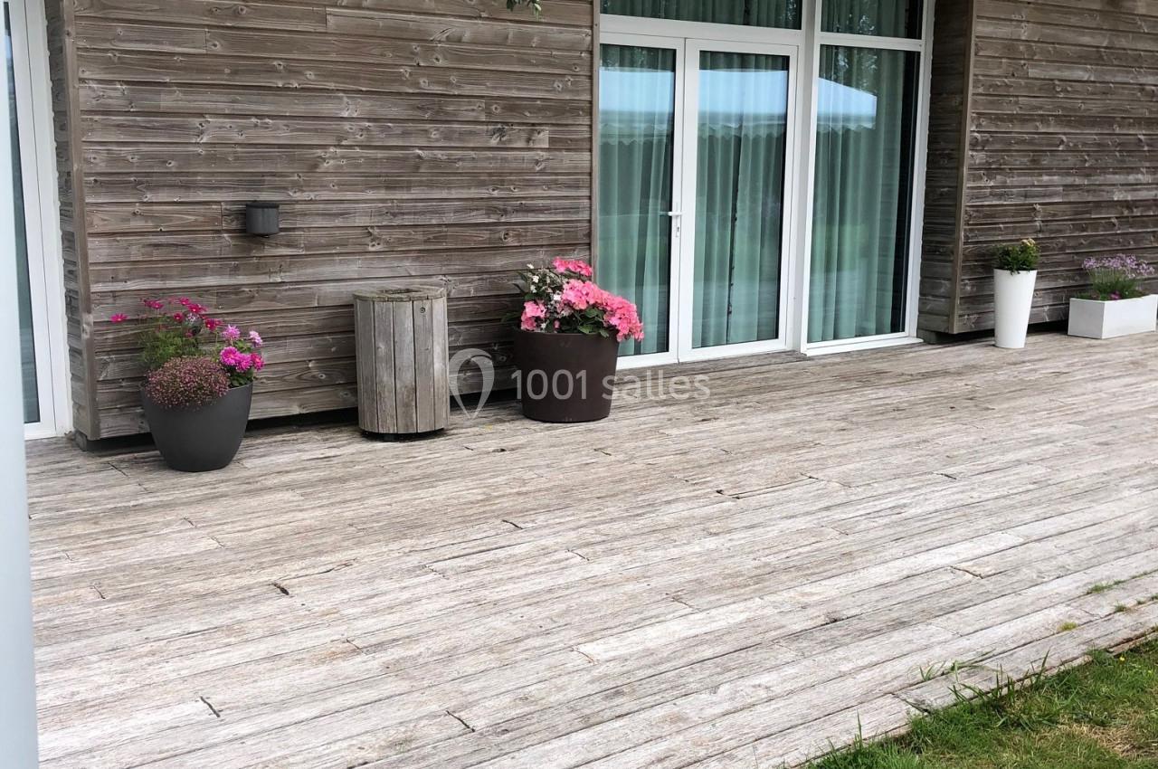 Terrasse en bois avec pots de fleurs, pergola en bois et grandes baies vitrées donnant sur l'intérieur.