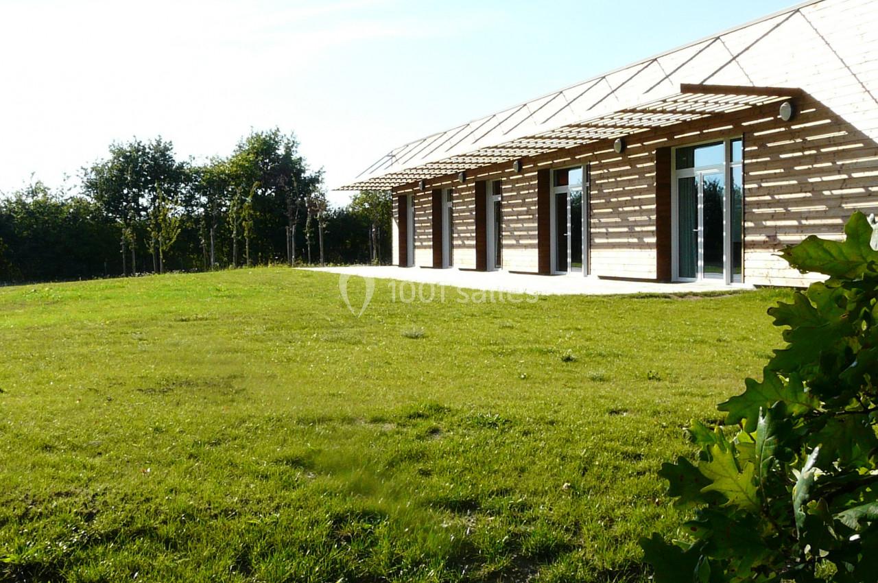 Bâtiment en bois avec de grandes baies vitrées, entouré d'une pelouse et d'arbres sous un ciel dégagé.