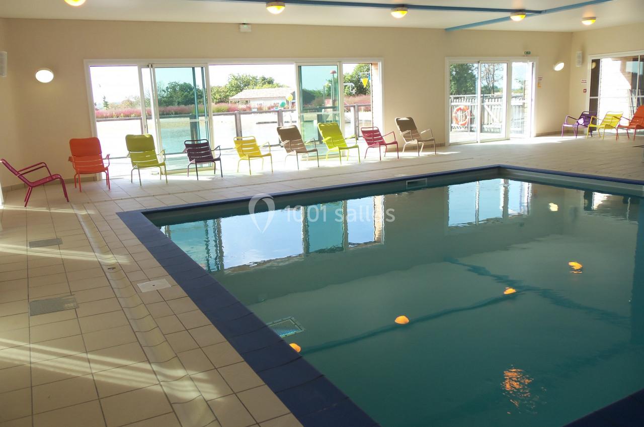 Piscine intérieure lumineuse avec chaises colorées alignées près des baies vitrées donnant sur un espace extérieur.