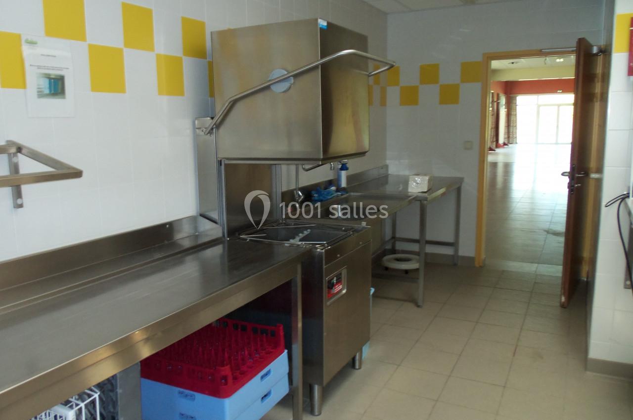 Cuisine professionnelle avec plan de travail en inox, lave-vaisselle industriel et casiers de rangement colorés.