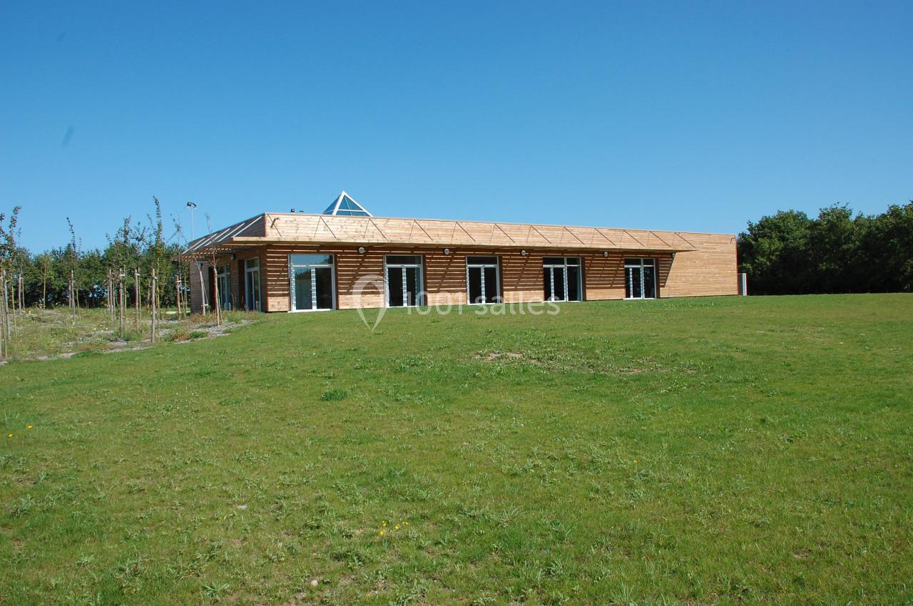 Bâtiment en bois à un étage avec de grandes baies vitrées, entouré d'une pelouse et d'arbres sous un ciel bleu.