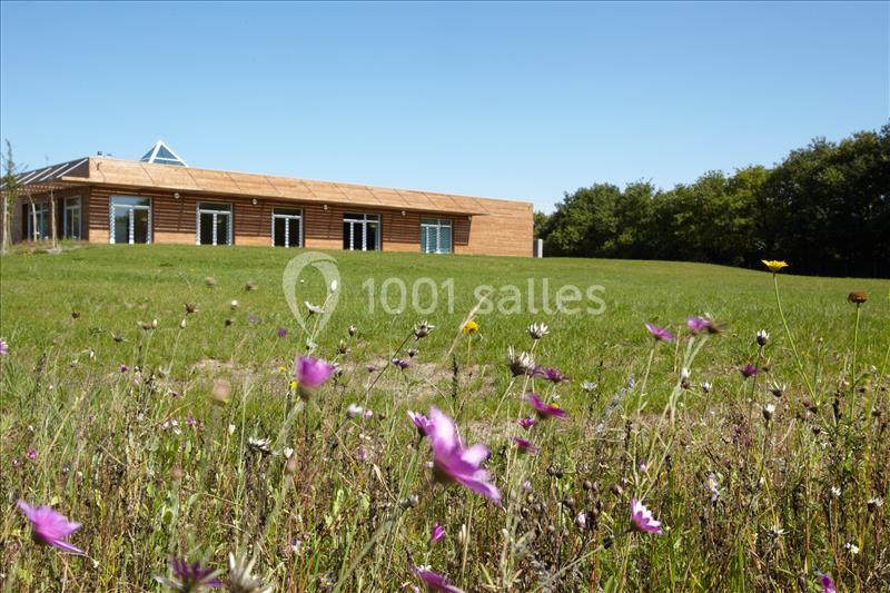Bâtiment en bois moderne entouré d'une prairie fleurie et d'une pelouse sous un ciel bleu.