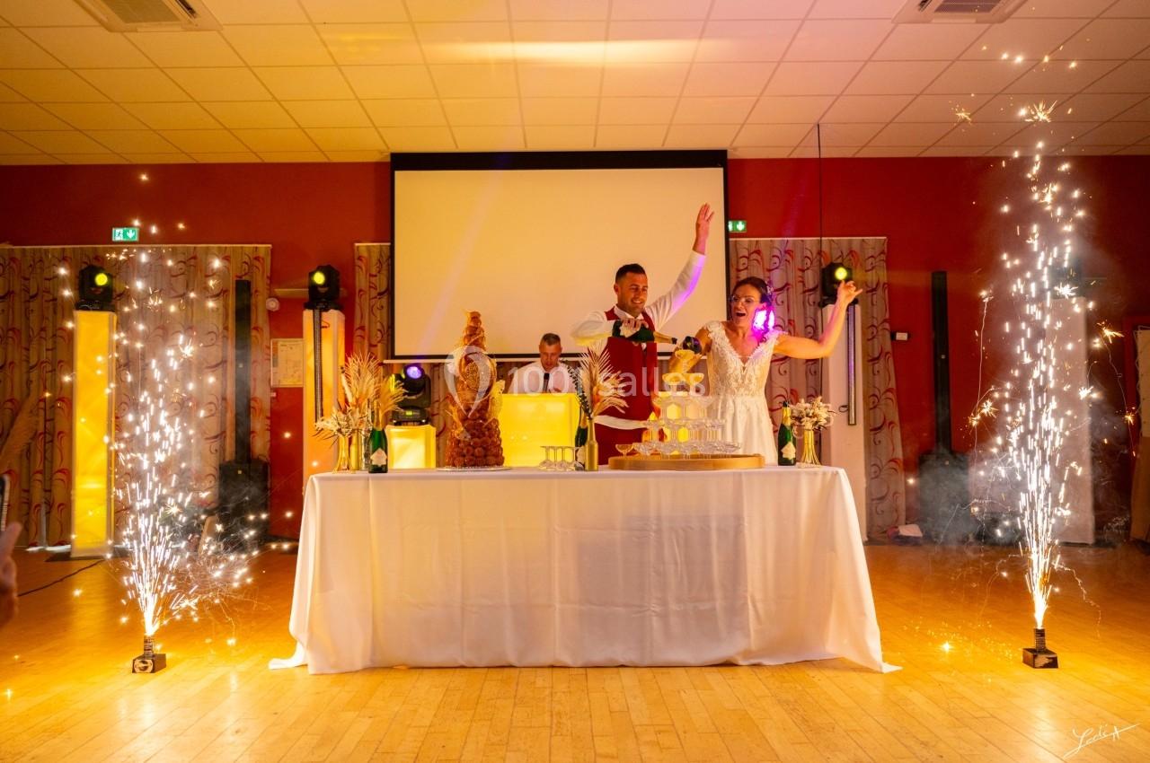 Un couple debout derrière une table décorée, entouré de fontaines d'étincelles dans une salle de réception.