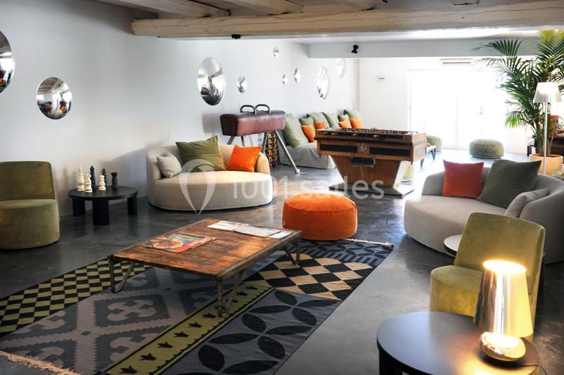 Salle lumineuse avec canapés, fauteuils colorés, baby-foot, tables basses et décorations modernes.