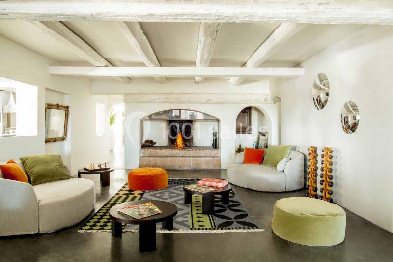 Salon lumineux avec cheminée allumée, poutres apparentes, mobilier coloré et décoration contemporaine.