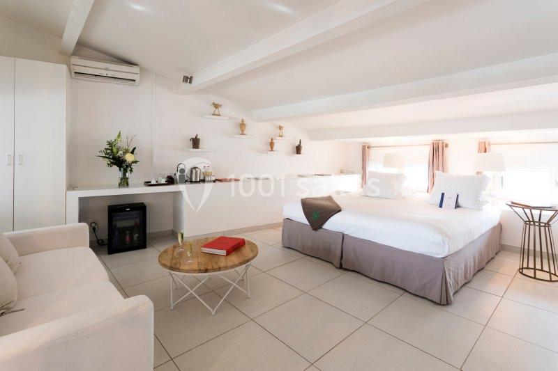 Chambre lumineuse avec lit double, canapé, table basse, kitchenette équipée et décoration minimaliste.