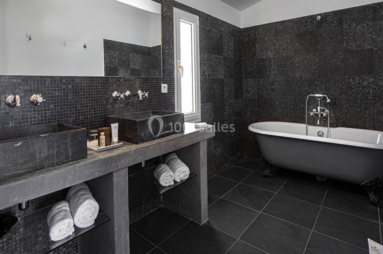 Salle de bain moderne avec carrelage noir, double vasque en pierre, baignoire sur pieds et fenêtre étroite.