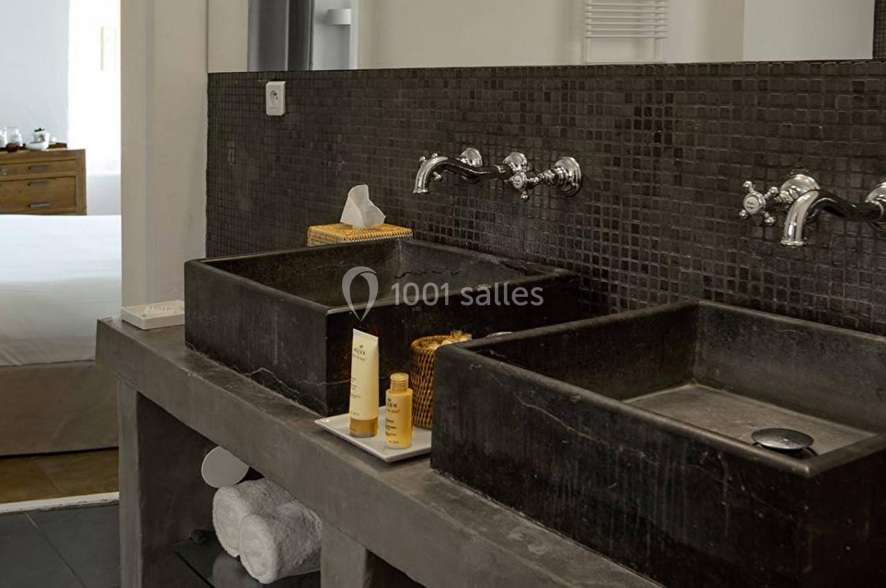 Deux lavabos noirs en pierre avec robinetterie murale, posés sur un plan en béton, dans une salle de bain moderne.