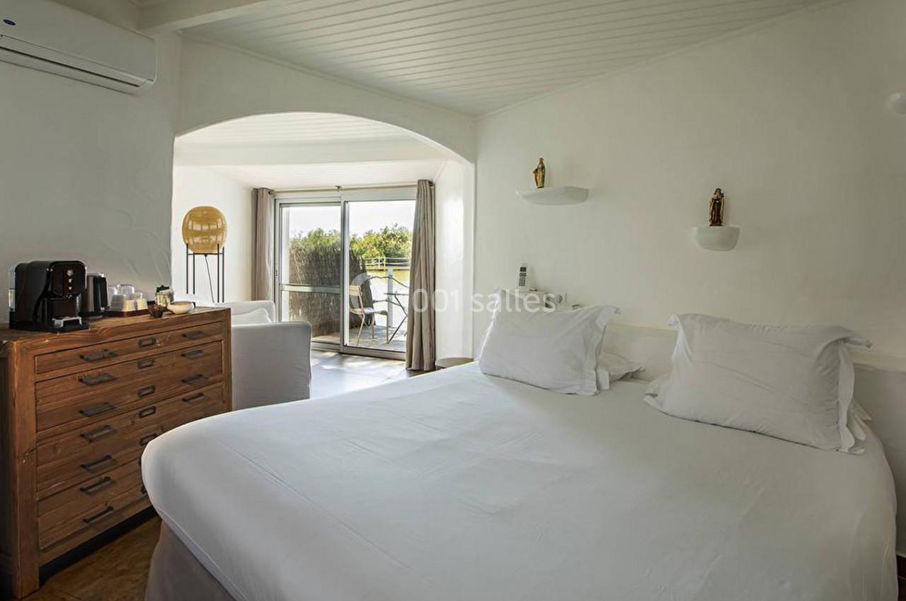 Chambre lumineuse avec lit double, commode en bois, machine à café et balcon donnant sur un paysage verdoyant.