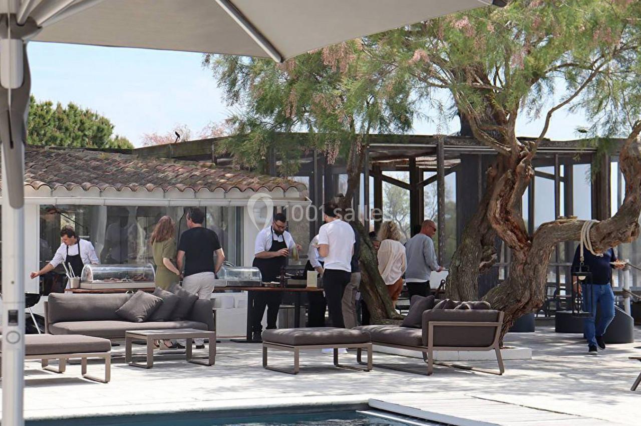 Personnes réunies autour d'un buffet en extérieur près d'une piscine, avec des meubles de jardin et des arbres en arrière…