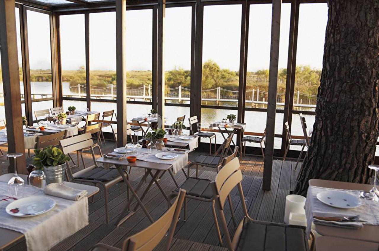 Salle de restaurant lumineuse avec baies vitrées donnant sur un paysage naturel et des tables dressées.