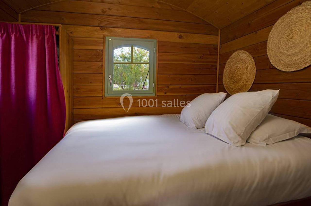 Lit double avec draps blancs dans une chambre en bois, décorée de paniers muraux et d'un rideau rouge.