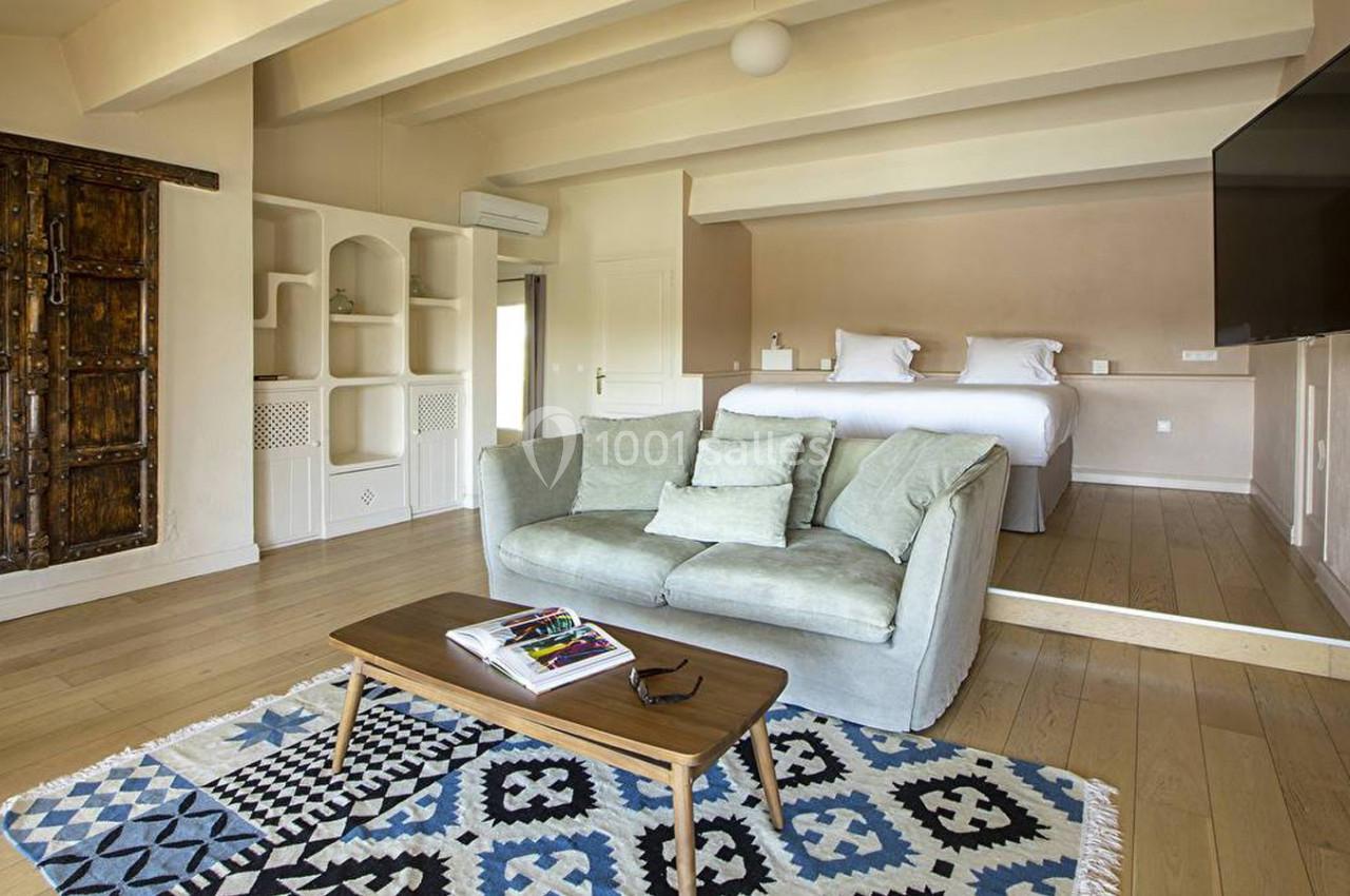 Salon lumineux avec canapé, table basse, tapis à motifs, et lit en arrière-plan dans une pièce au décor épuré.