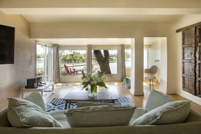 Salon lumineux avec canapé, table basse, tapis à motifs, et chambre en mezzanine avec lit double en arrière-plan.