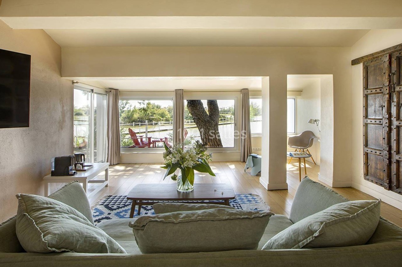 Salon lumineux avec canapé, table basse, bouquet de fleurs, grande baie vitrée donnant sur une terrasse et vue extérieure.
