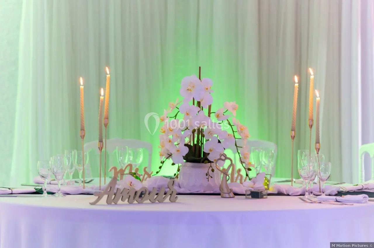 Table décorée pour un événement avec des bougies, des orchidées blanches et un panneau ’Amour’ sur une nappe blanche.