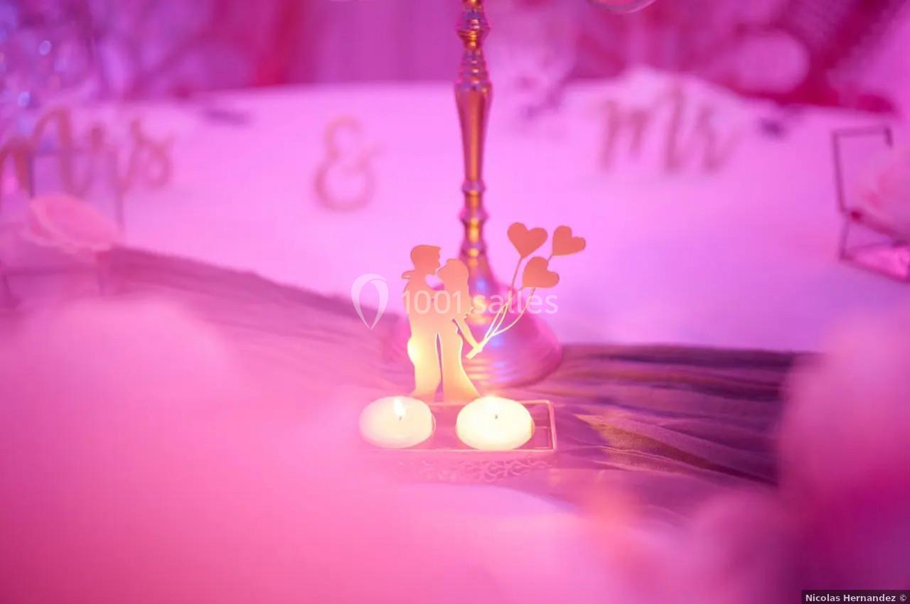 Décoration romantique avec une silhouette de couple, deux bougies allumées et un fond rose flou.