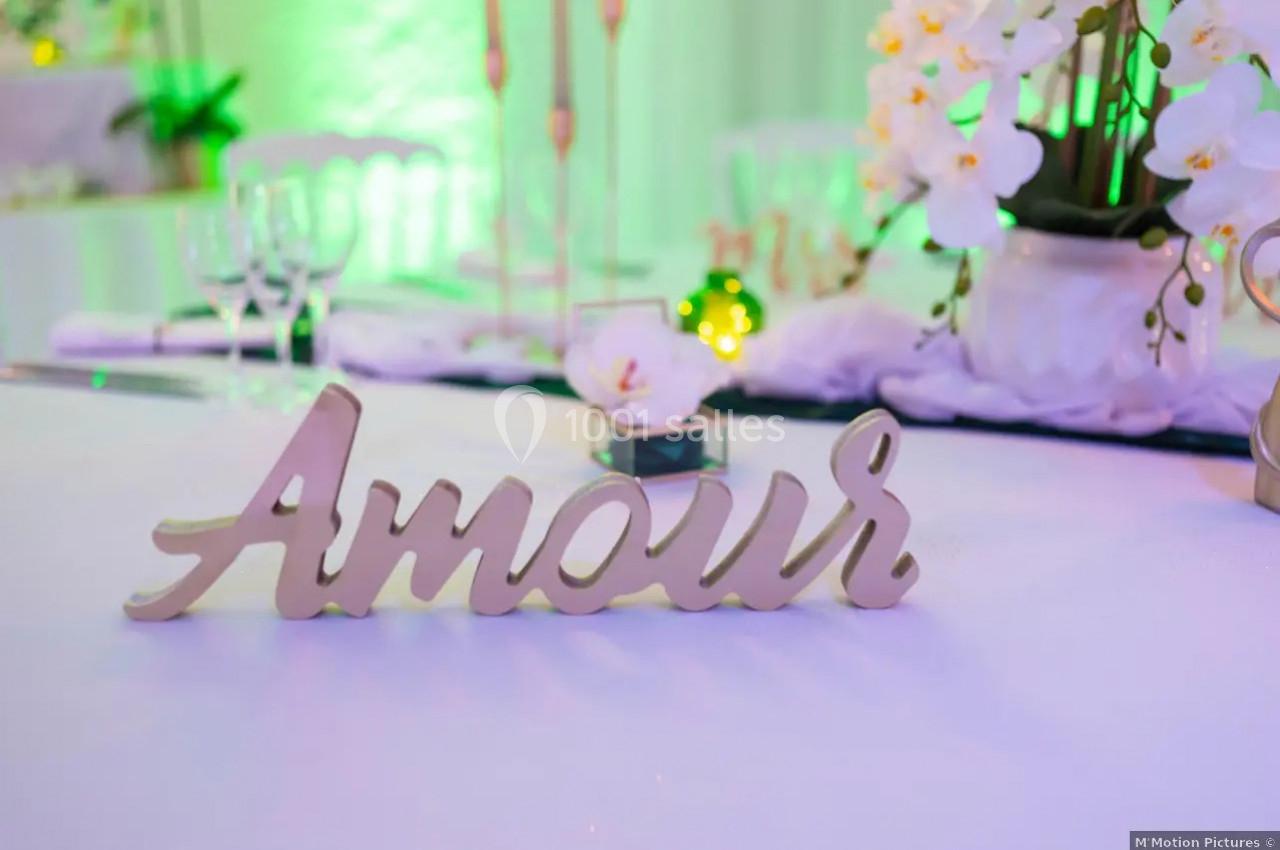 Décoration de table avec le mot ’Amour’ en bois, des fleurs blanches et une ambiance lumineuse verte.