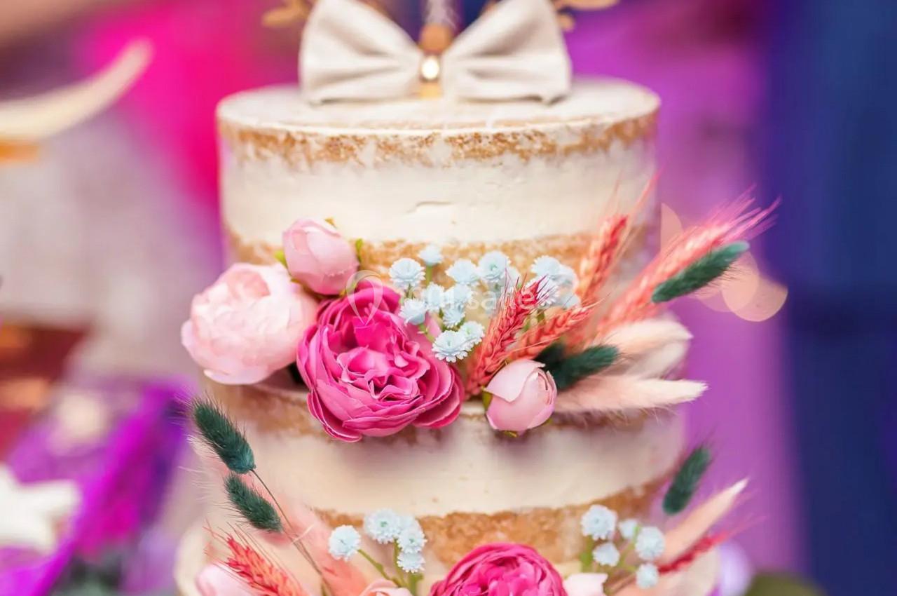 Gâteau de mariage à trois étages décoré de fleurs roses et séchées, avec un topper portant des prénoms.
