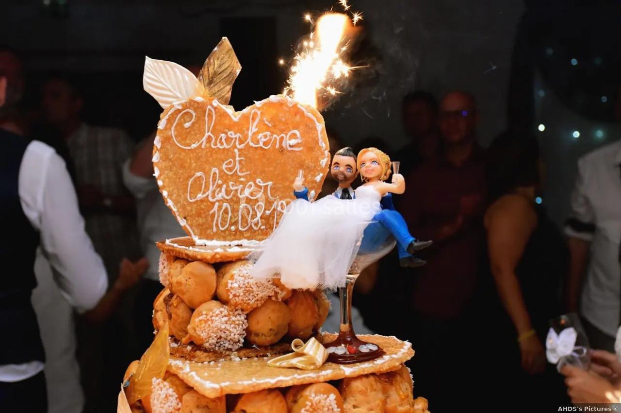 Pièce montée en choux avec figurines de mariés et une inscription en sucre, décorée d'une étincelle allumée.