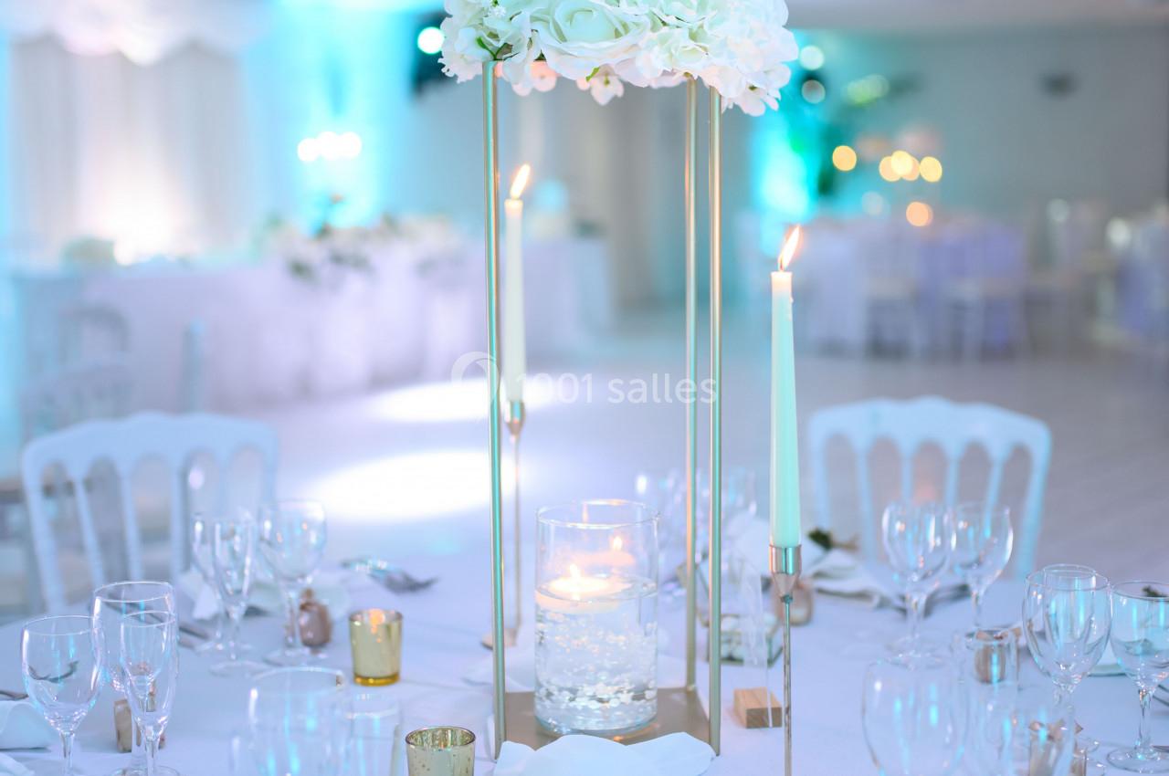 Table de réception élégamment dressée avec un centre de table floral blanc, bougies et vaisselle raffinée.