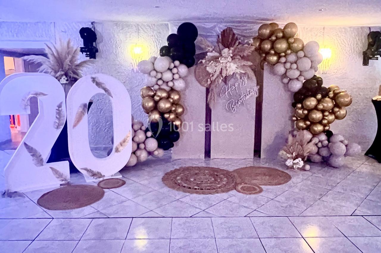 Décoration festive avec ballons dorés et blancs, chiffre ’20’ en grand, et panneau central orné de fleurs.