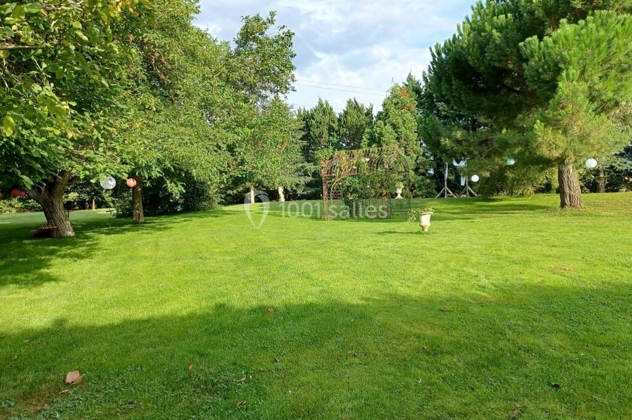 Pelouse verdoyante avec des arbres, une arche décorative et des lanternes suspendues dans un jardin ensoleillé.