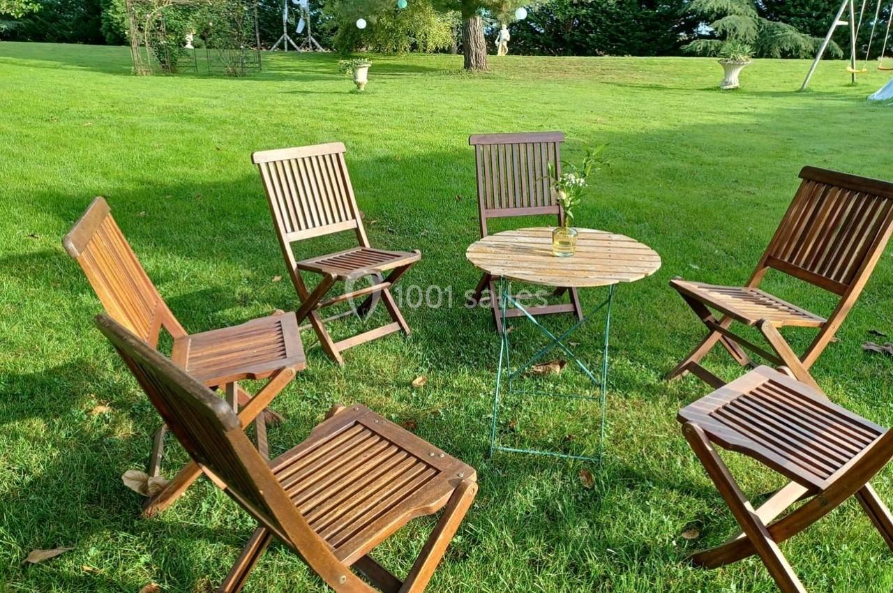 Chaises en bois disposées autour d'une petite table ronde avec un vase, sur une pelouse ensoleillée.