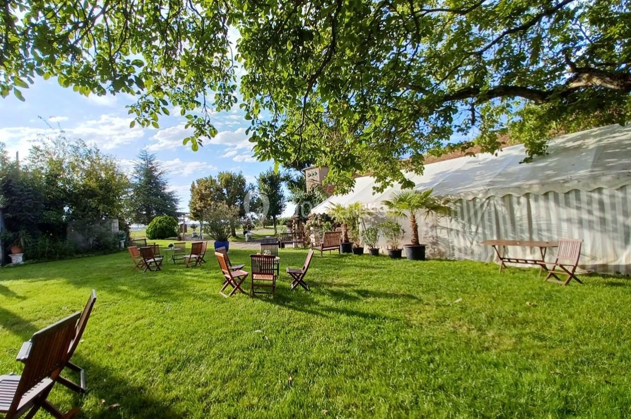 Chaises et tables en bois disposées sur une pelouse verdoyante, sous des arbres, près d'une grande tente blanche.