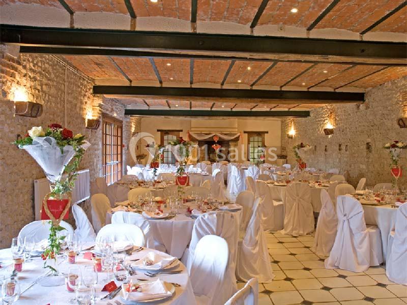 Salle de réception décorée avec des tables rondes, nappes blanches, chaises habillées et arrangements floraux.