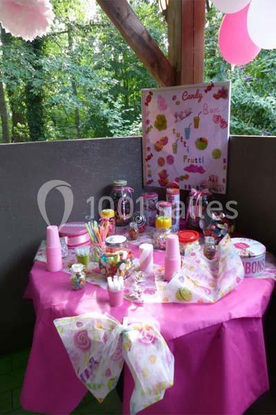 Table décorée avec une nappe rose, garnie de bonbons, accessoires colorés et décorations festives, en extérieur.