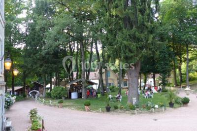 Deux fauteuils en rotin décorés, placés sous une arche ornée de fleurs et de tissus, dans un jardin verdoyant.
