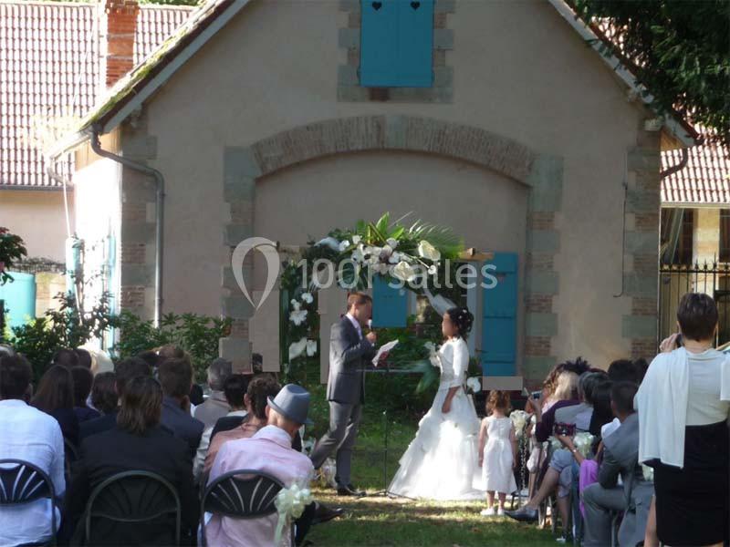 Un couple échange ses vœux devant une arche fleurie lors d'une cérémonie de mariage en extérieur.