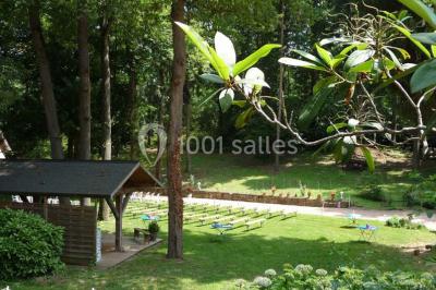 Deux fauteuils en rotin décorés, placés sous une arche ornée de fleurs et de tissus, dans un jardin verdoyant.