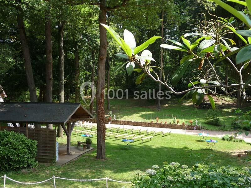 Vue d'un jardin verdoyant avec des bancs alignés, une petite cabane en bois et des arbres en arrière-plan.
