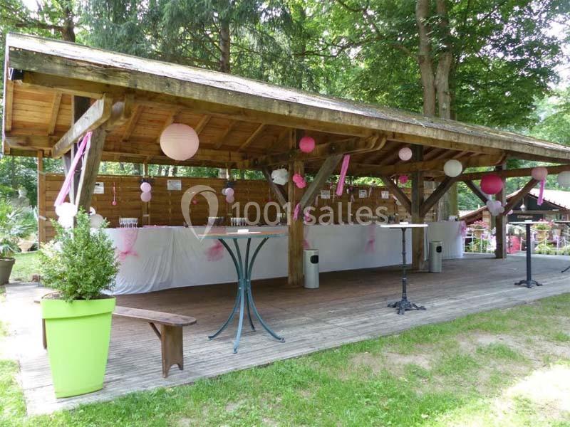 Abri en bois décoré de lanternes et guirlandes roses, avec tables et bancs sur une terrasse en plein air.